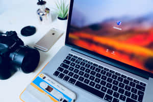 筆記型電腦帶有日落壁紙，旁邊是相機和卡式錄音帶在桌子上。 — MacBook Air M3 壁紙