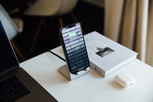 智能手機在支架上充電，旁邊有手提電腦和AirPods，放在乾淨的桌子上。 — MacBook Air 15 壁紙