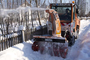 橙色吹雪機喺冬天沿住木籬笆清理積雪。 — MacBook Pro 壁紙