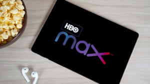平板電腦帶有HBO Max標誌，旁邊有爆谷和耳塞，在木桌上。 — 螢幕保護 壁紙