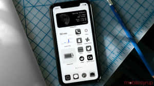智能手機顯示月相和應用程式，在藍色網格墊上，鉛筆在附近。 — 美學 iPhone 壁紙
