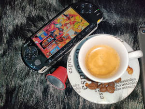PSP遊戲機連動畫遊戲，旁邊有濃縮咖啡杯，置於毛絨表面上。 — PlayStation GIF 壁紙