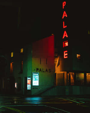 夜晚中，Palace Cinema 閃爍的紅色霓虹燈招牌，以及濕漉漉的街道反射出五彩繽紛的燈光。 — 氛圍 GIF 壁紙