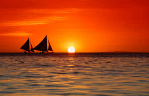 兩艘帆船在平靜的水面上，以鮮豔的橙色夕陽為背景形成剪影。