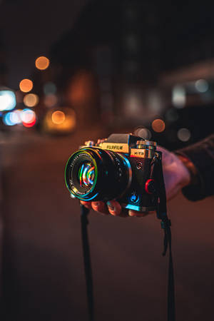 夜晚手持 Fujifilm X-T3 相機，背景城市燈光模糊。 — 相機 壁紙