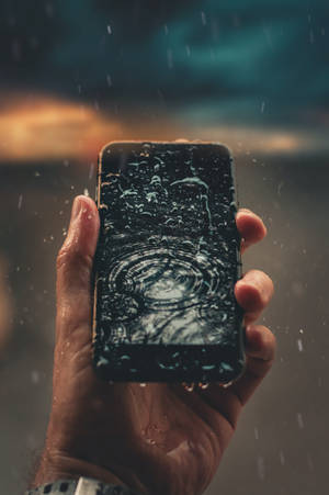 手在雨中握著濕手機，背景有日落 — 雨天 壁紙