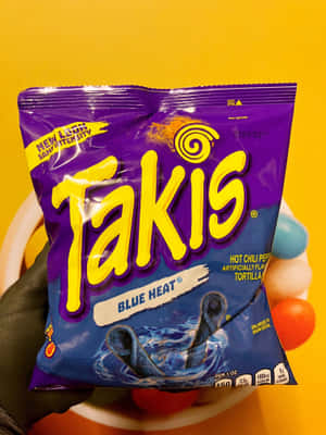 手拎住一袋Takis Blue Heat零食粟米片，背景係黃色。 — 3:4 壁紙