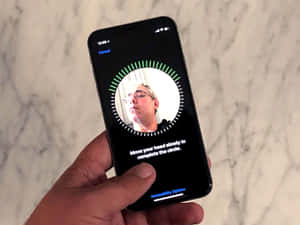 手拿著手機，在大理石表面上具有面部追蹤功能。 — iPhone 鎖定畫面 GIF 壁紙
