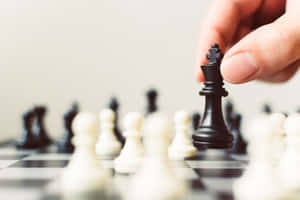 手將黑色國際象棋國王舉起在帶有模糊棋子的棋盤上方。 — 國際象棋 壁紙