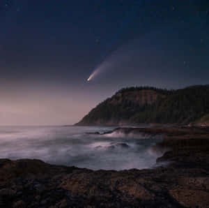 彗星劃過繁星點點的夜空，籠罩在霧氣中的海洋和樹木繁茂的懸崖之上。 — 月色夜空 壁紙