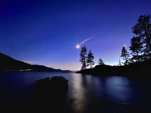 彗星在暮色天空中閃耀，湖泊上有樹木剪影和遠山。 — 夜景城市 壁紙