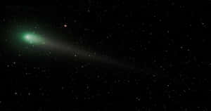 一顆帶有發光尾巴的綠色彗星在佈滿星星的夜空中移動。 — 月色夜空 壁紙