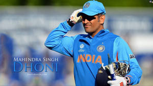 板球運動員 Mahendra Singh Dhoni 穿著藍色印度制服脫帽致意，手持球棒和頭盔。 — 巴基斯坦板球 壁紙