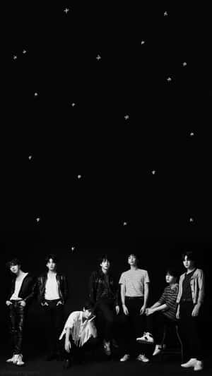 七位穿著休閒服的年輕男性在黑白星空下擺姿勢。 — 防彈少年團 合照 壁紙