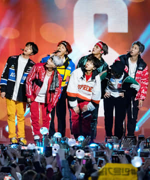 七位男K-pop偶像在舞台上表演，粉絲們高舉手機。 — Apple Watch Ultra 壁紙