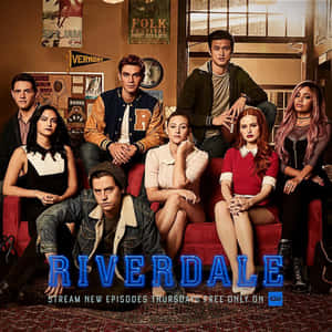 七名《Riverdale》青少年在裝飾有節目標題的房間裡的紅色沙發上擺姿勢。