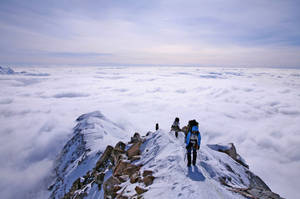 登山者在廣闊雲海之上的積雪山脊上徒步。