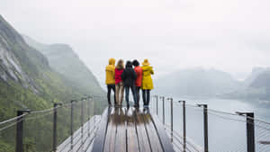 四個人穿著雨衣站在橋上，眺望峽灣和山脈。
