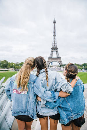三位身穿牛仔外套的女孩擁抱並看著艾菲爾鐵塔。