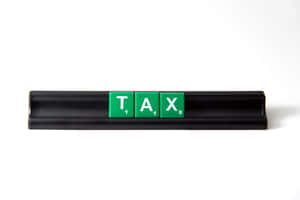 綠色 Scrabble 字母牌在黑色底座上拼出 TAX，白色背景。 — MacBook Air M3 壁紙