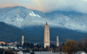三座塔矗立在白雪覆蓋的山脈前，天空多雲。 — 中國 壁紙