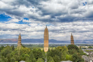 三座金色寶塔被樹木環繞，背景有山脈和多雲的天空。 — 中國 壁紙