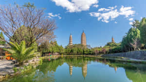 三座塔倒映在寧靜的池塘中，周圍有樹木和藍天。 — 風景動圖 壁紙