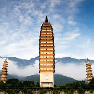 三座石塔高聳入雲，背景是霧氣繚繞的山巒和部分多雲的天空。 — 建築 壁紙