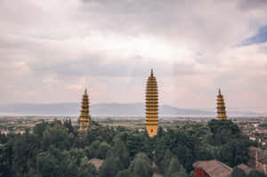 三座金色寶塔被樹木環繞，遠山在陰天下。 — 中國 壁紙