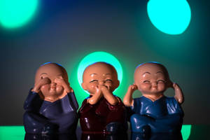 三個陶瓷僧侶雕像在發光的青綠色燈光下遮住眼睛、耳朵和嘴巴。
