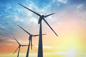 三座風力發電機在色彩繽紛的日落天空襯托下呈現剪影。 — 明亮 壁紙