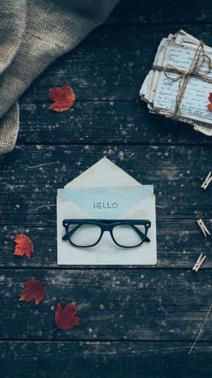 眼鏡在寫有'hello'的信封上，周圍是秋葉和綁著的信件在木頭上。