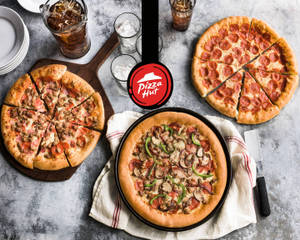 三款 Pizza Hut 薄餅配飲品，放喺灰色枱上。 — 薄餅 壁紙