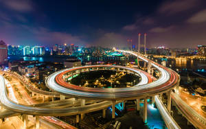 夜晚閃爍的高速公路交匯處，移動車輛的光跡和背景的城市天際線。