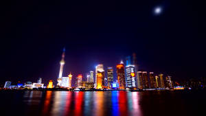 夜景，發光的城市天際線倒映在水中，上方有月亮。 — 唐人街 GIF 壁紙