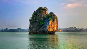 一個長滿綠樹的大岩石島嶼，在日落時分矗立在平靜的水中。
