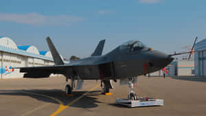 灰色戰鬥機停在機場停機坪，靠近機庫，藍天背景