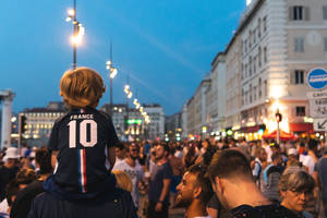 穿著法國10號球衣的小孩在黃昏擁擠的城市街道上坐在肩膀上。