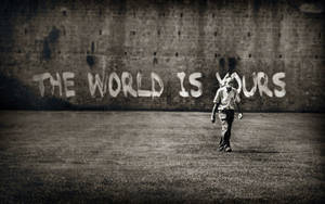 男人在塗鴉牆下走向觀眾，牆上寫著「The World Is Yours」