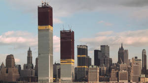 在密集的城市天際線中，兩座正在建設中的摩天大樓，天空中有雲。