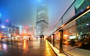 夜晚的現代城市天際線，潮濕的路面反射著霓虹燈光和霧氣瀰漫的氛圍。 — 唐人街 GIF 壁紙