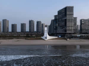 沙灘上的白色現代紀念碑，背景是暮色中的城市天際線