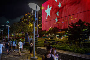 夜間城市場景，人們走過建築物上大型的旗幟燈光展示。 — 中國 壁紙