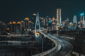 夜晚在密集城市中，一座彎曲的發光橋樑，伴隨著發光的摩天大樓和光跡。 — 夜景城市 壁紙