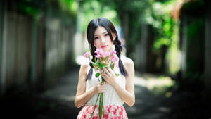 年輕女子在陽光明媚的花園小徑上手持粉紅玫瑰。