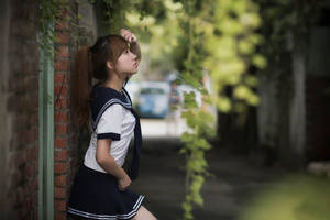 一個穿著水手服的女孩在綠樹成蔭的小巷裡靠著磚牆。