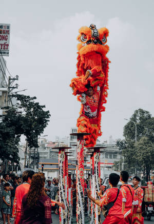 穿著紅色服裝的表演者在街頭慶祝活動中，在高桿上平衡一個大型橙色舞獅木偶。