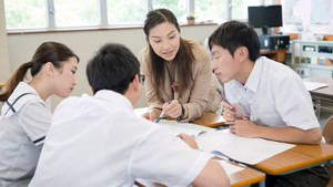 老師在課室書桌前幫助學生學習。 — 中文 壁紙