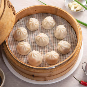竹蒸籠裡新鮮嘅餃子配蒜頭、蔥花同辣椒。