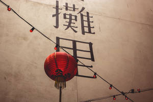 紅色燈籠帶流蘇掛在帶有中文字和燈串的牆前。